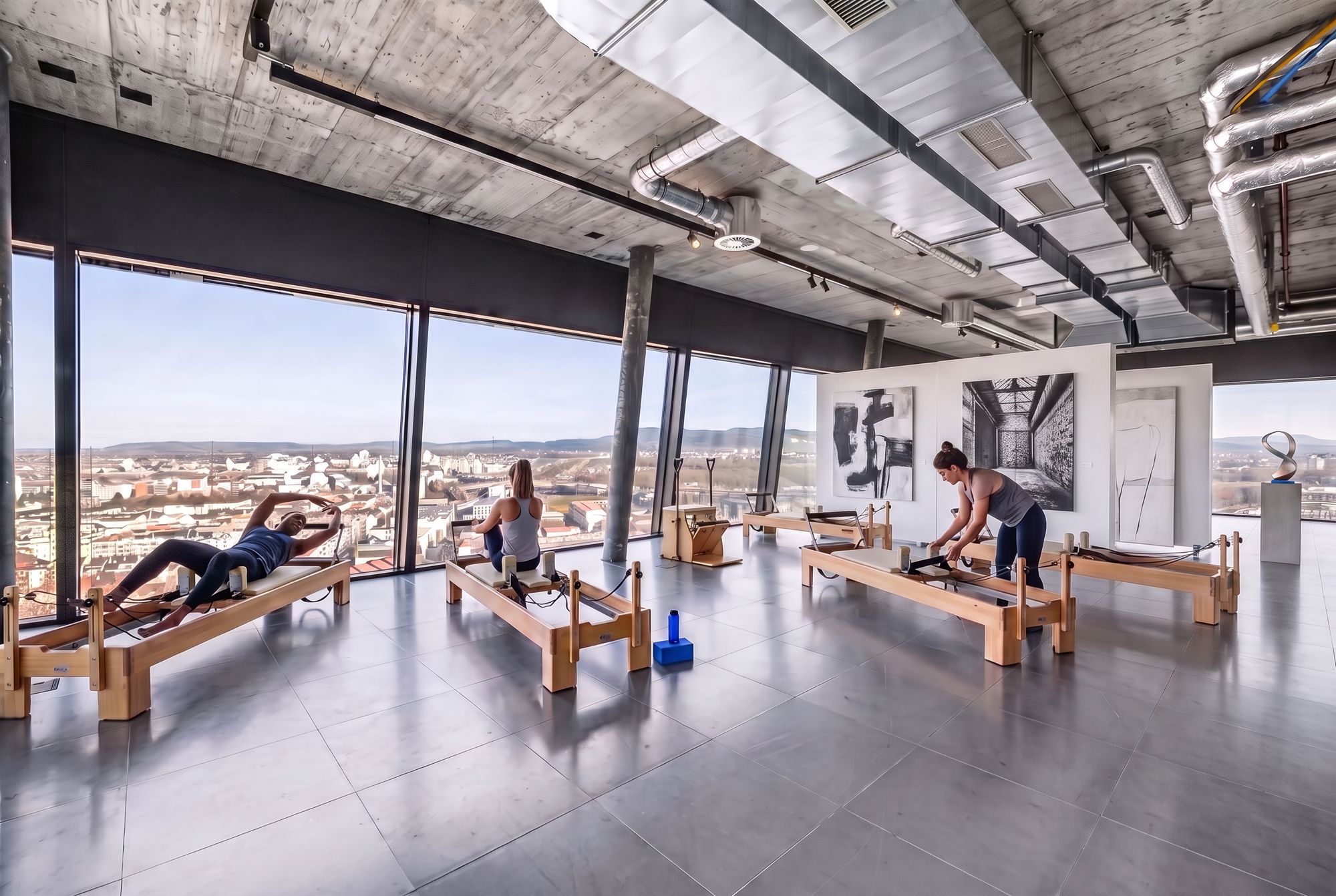 Reformer-Session am Morgen mit Eichengeräten, drei Trainierenden und grossformatiger Kunst auf einer Ausstellungstafel im hellen Hauptraum